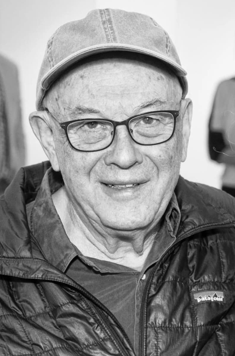 B&W portrait of Bruce Davidson looking into the camera and wearing a baseball cap, glasses, and a Patagonia jacket