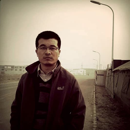 Color half-length portrait of Song Chao with street background wearing wireframe glasses a sweater and a jacket