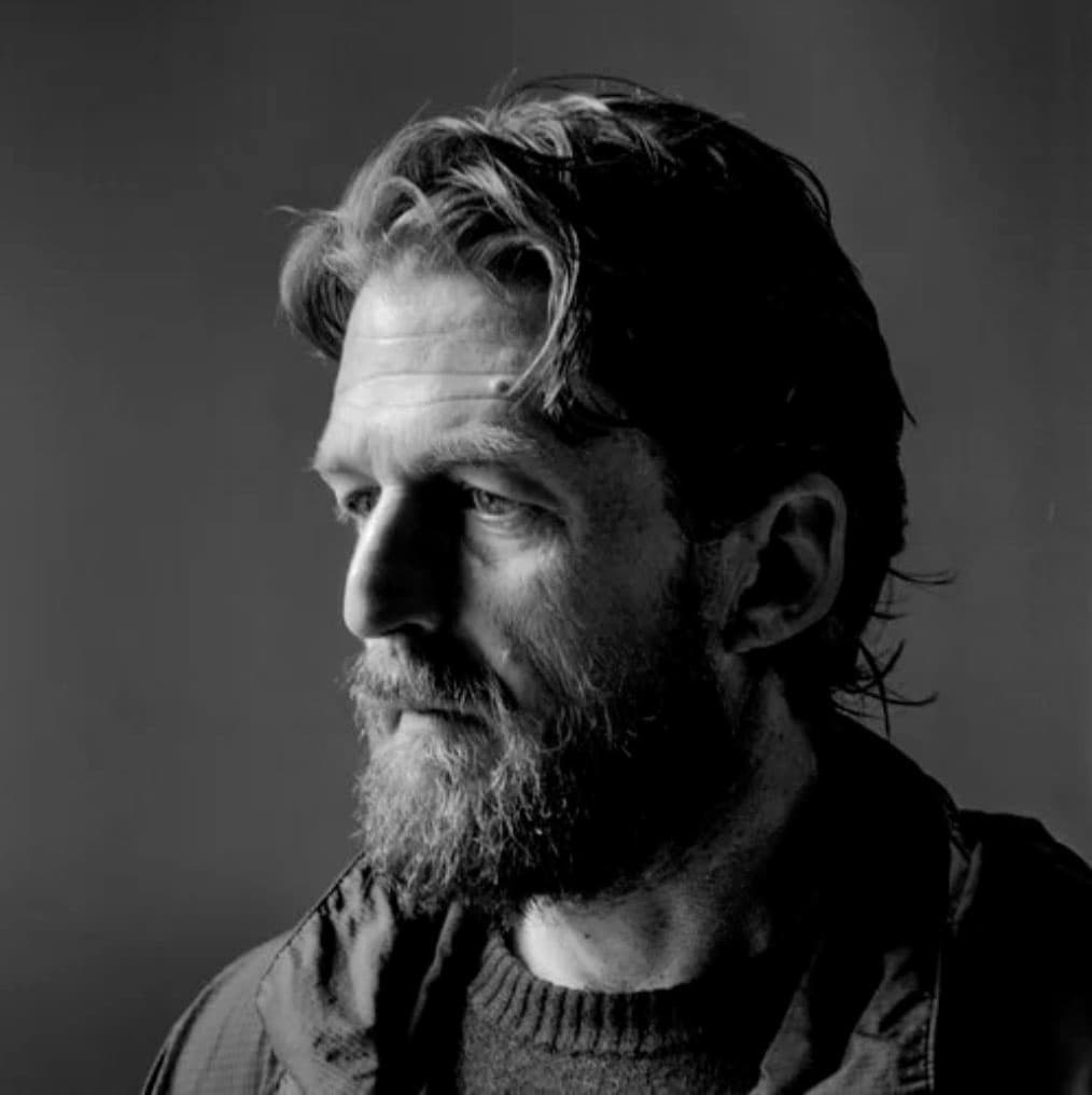 B&W portrait of Matt Black looking to the left wearing a sweater and jacket