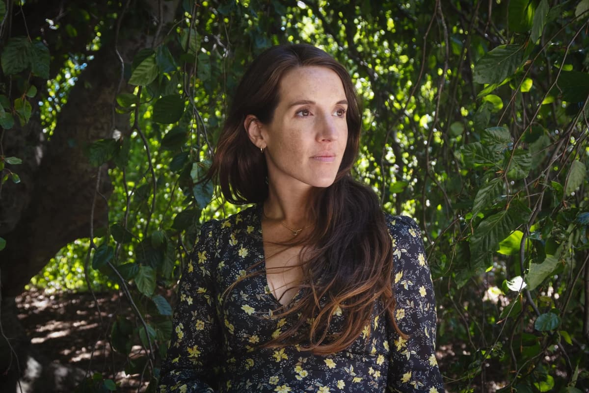 Color portrait of Nichole Sobecki surrounded by greenery wearing a long-sleeved floral shirt