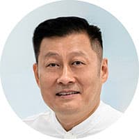 Color portrait of Wu Qi looking into the camera wearing a white shirt in front of a light blue background