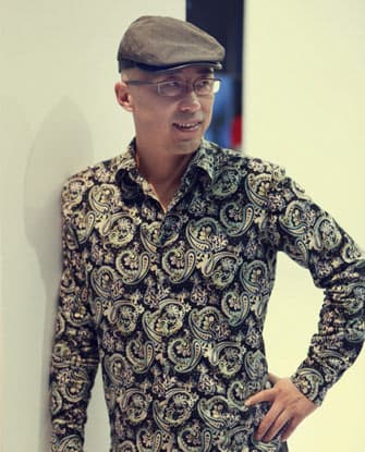 Color half-length portrait of Yang Shaobin wearing a hat, glasses, and a paisley button down shirt