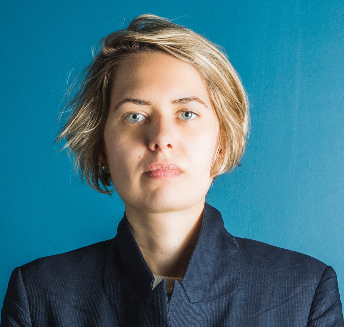 Color portrait of Anna Filipova in front of a blue background wearing a navy blue shirt