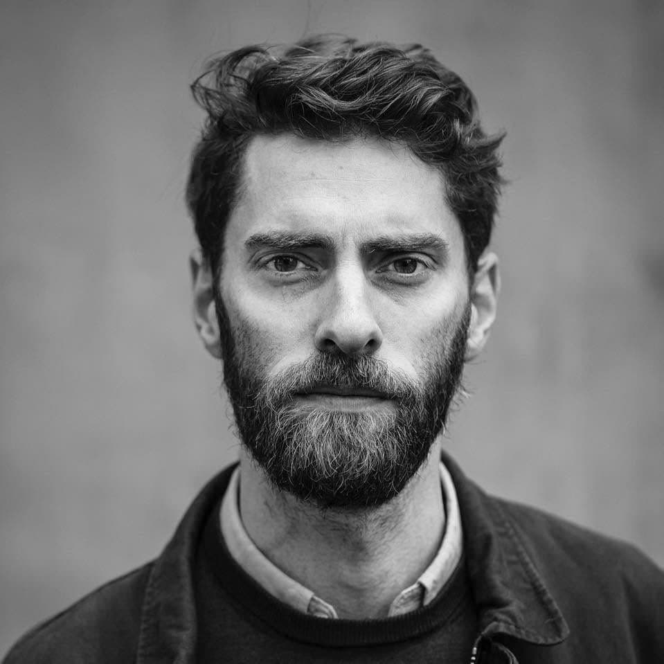 B&W portrait of Jonas Bendikson looking into the camera wearing a dark jacket in front of a grey background